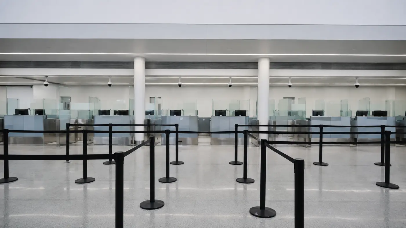 Empty border inspection hall with retractable queue barriers leading toward a row of officer booths