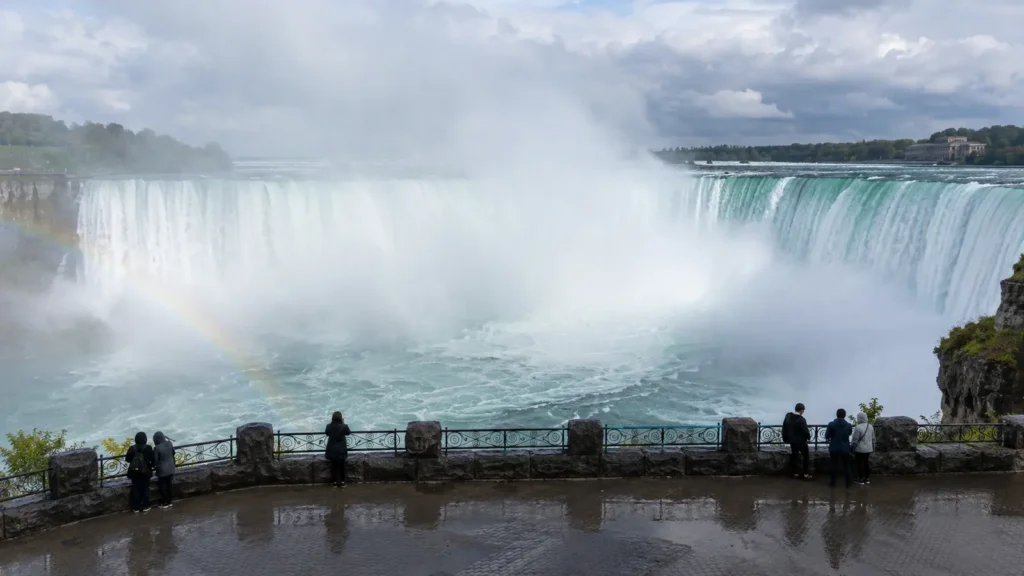 Wide curved waterfall throwing up mist, seen head-on from a railed viewpoint, the main sight on a Toronto to Niagara Falls day trip